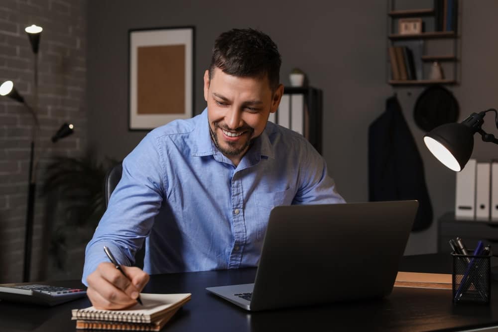 Man making notes while on laptop presenting online