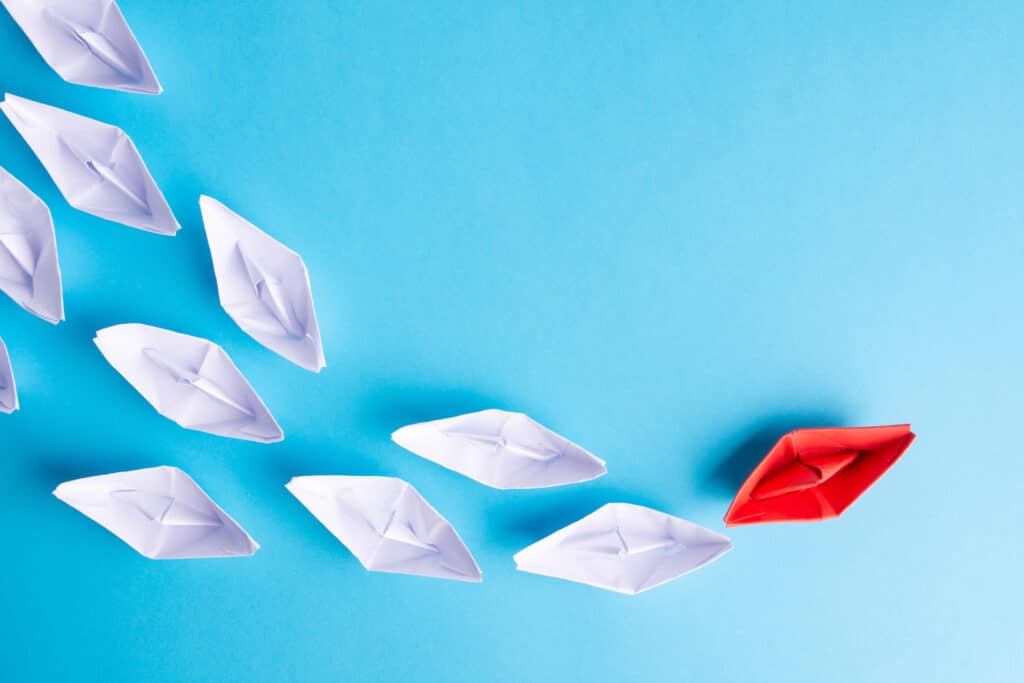 red origami boat in a sea of white origami boats